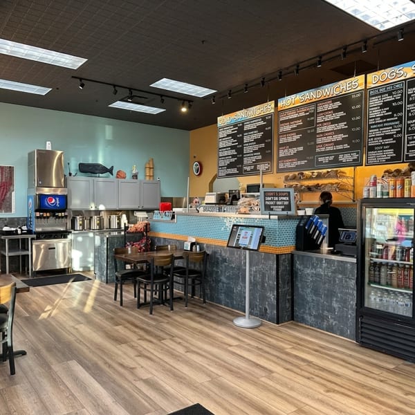 Interior view of a sandwich shop with menu boards, a counter, and seating area.