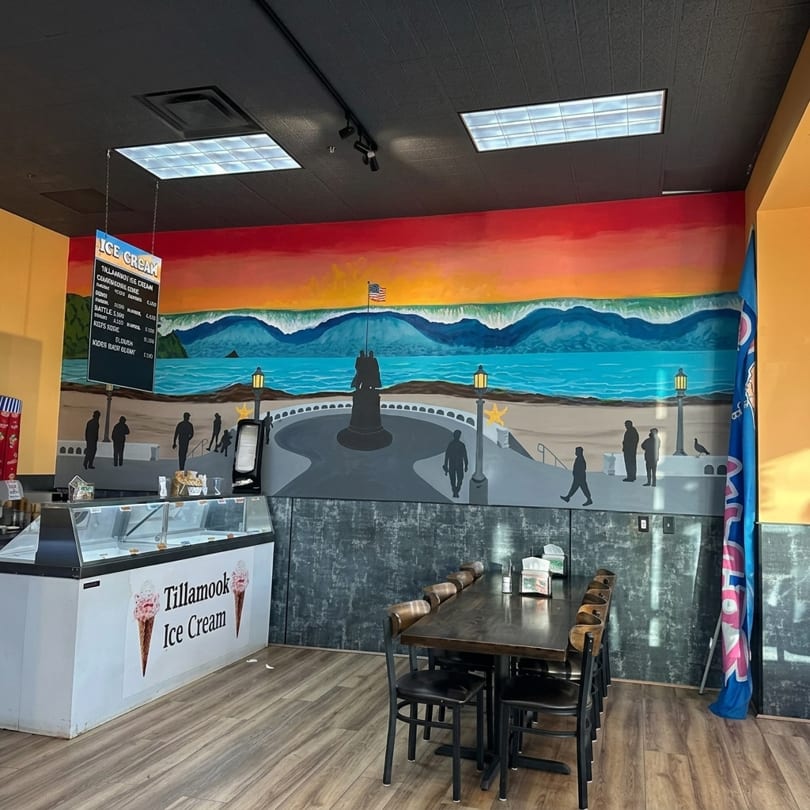 Tillamook Ice Cream shop interior with a vibrant mural of a coastal scene and a long dining table.