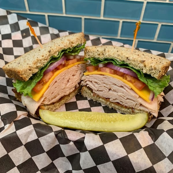 Turkey sandwich on whole wheat bread with cheese, lettuce, tomato, onion, and a pickle spear.